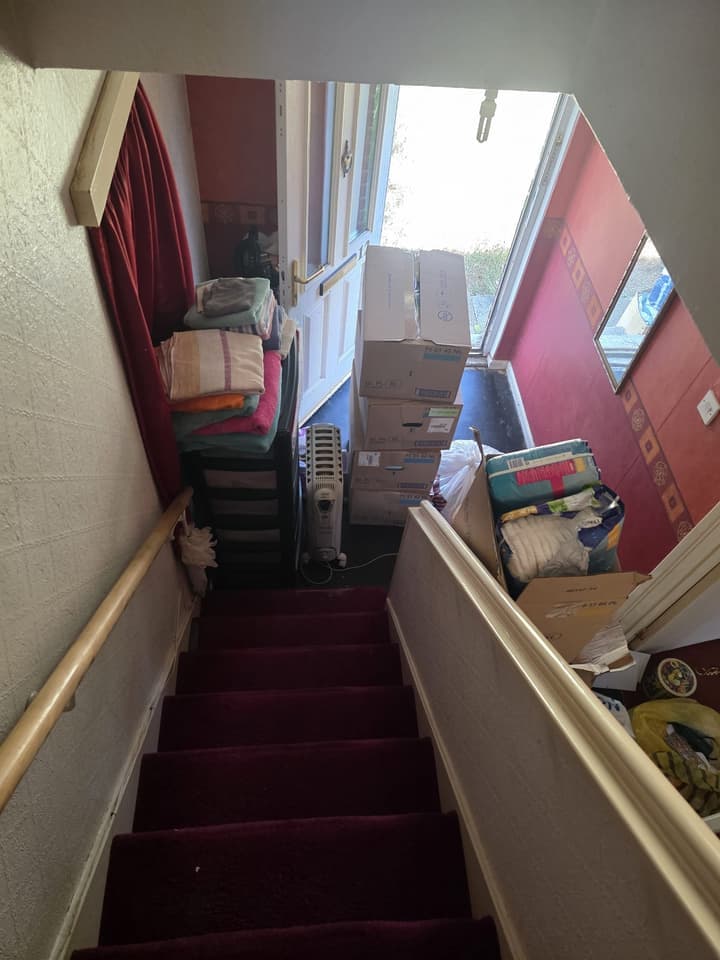 Stairs and hall before the clearance, with boxes and bedding stacked by the front door