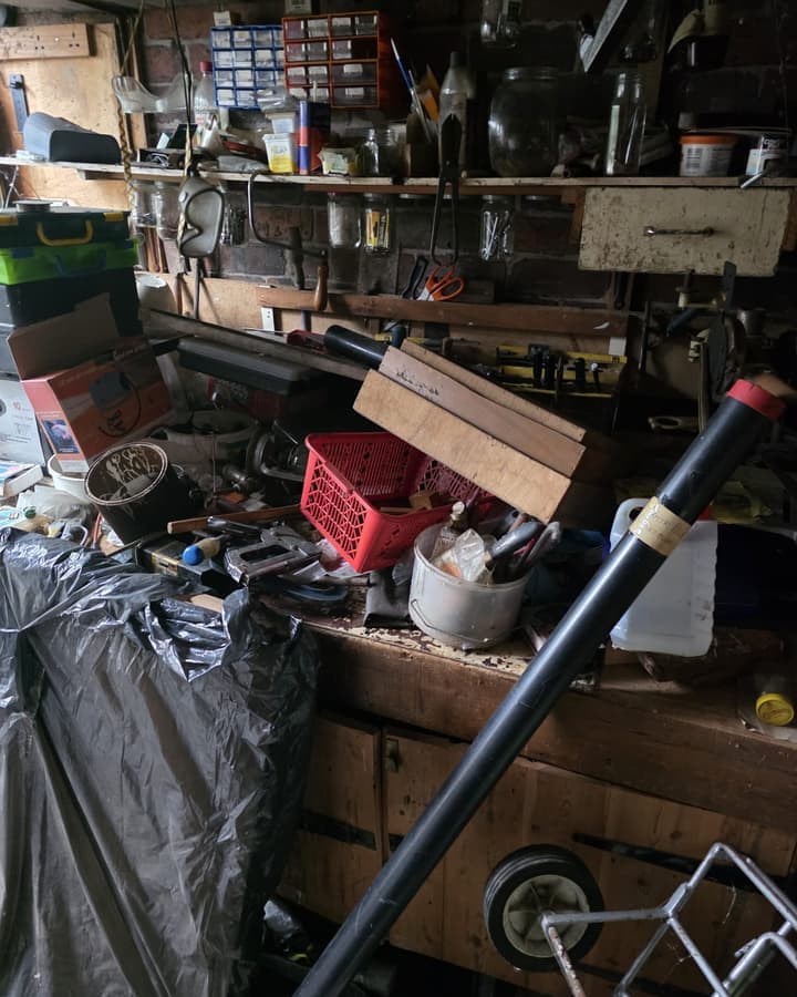 A garage workbench crowded with tools, tins and metal fittings